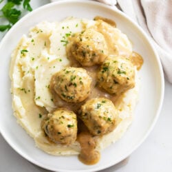 Chicken Meatballs and sauce on top of mashed potatoes on a white plate.