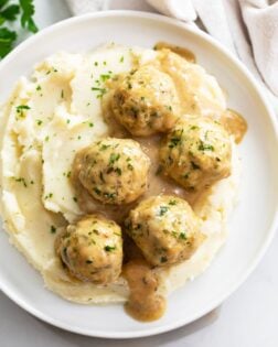 Chicken Meatballs and sauce on top of mashed potatoes on a white plate.