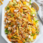 Chinese Chicken Salad on a white plate with lettuce, cabbage, chicken, mandarin oranges, and dressing.