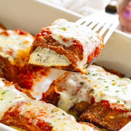 Eggplant Rollatini being pulled up from a casserole dish with a spatula.