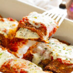 Eggplant Rollatini with ricotta filling being pulled up from a casserole dish by a spatula.