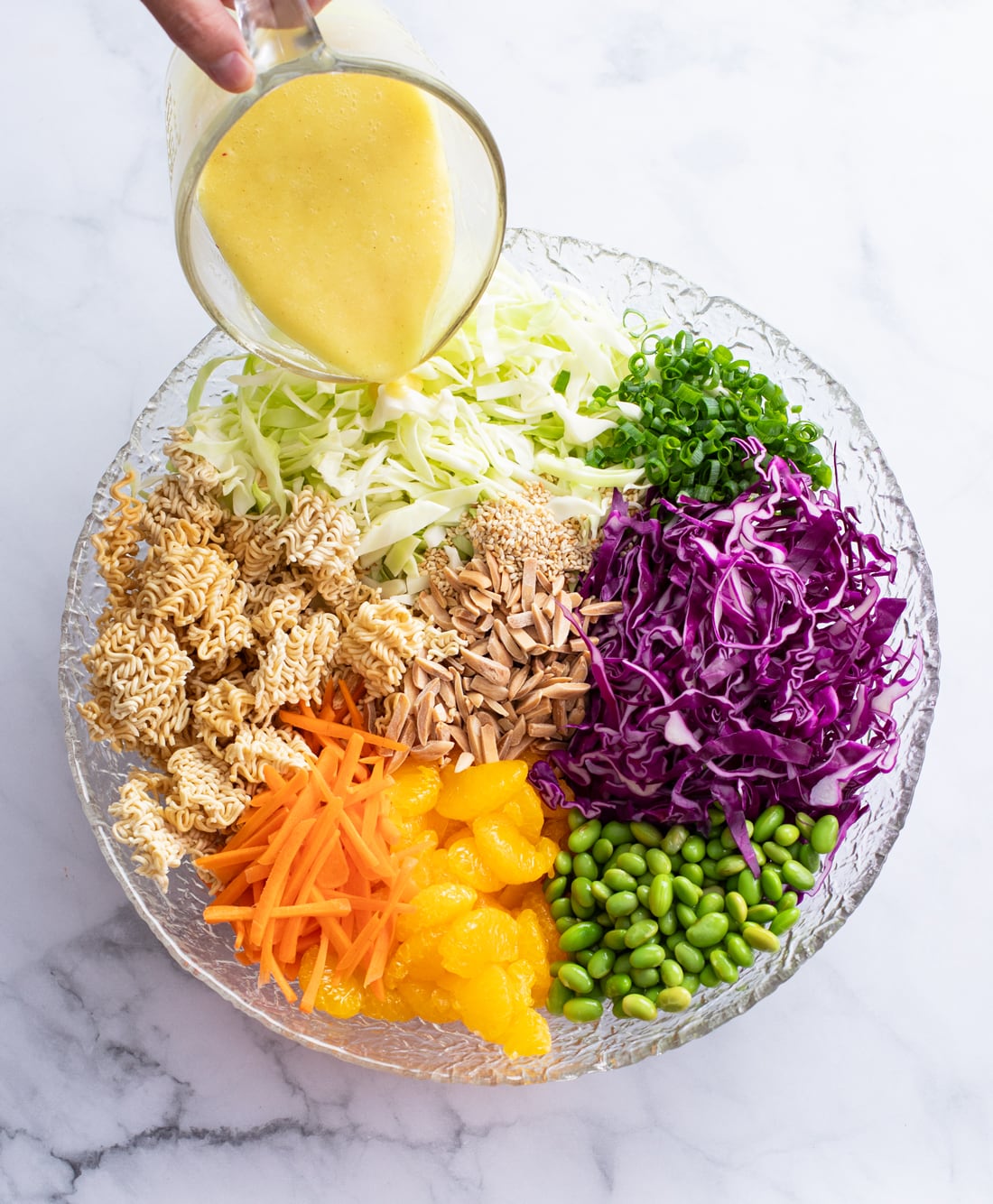 Ingredients for Ramen Noodle Salad in a large bowl with dressing being poured on top.