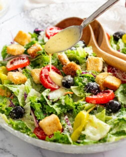 A bowl of Olive Garden Salad with a spoon drizzling salad dressing on top.