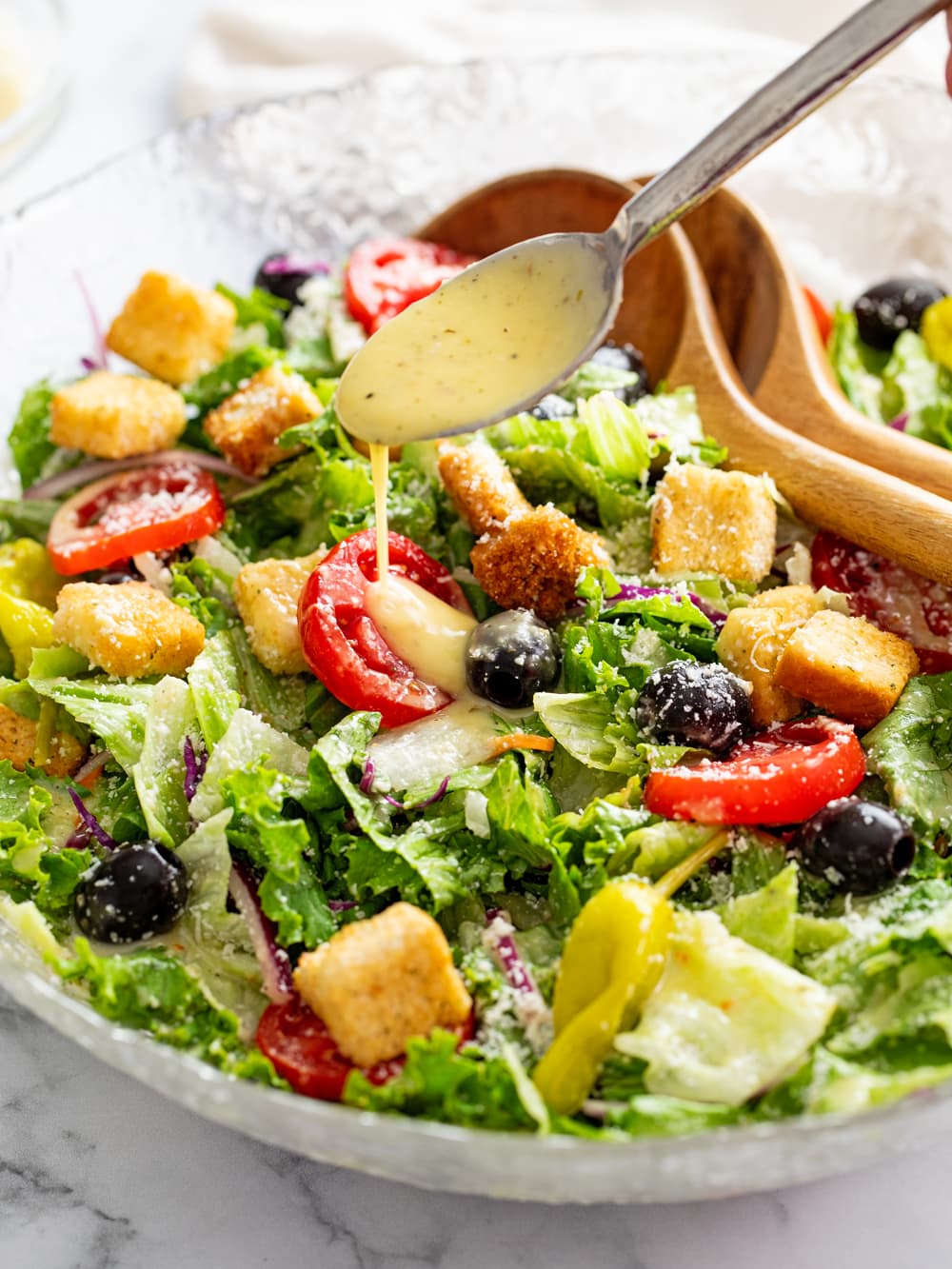 A bowl of Olive Garden Salad with a spoon drizzling salad dressing on top.