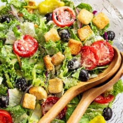 Olive Garden Salad in a glass bowl with wooden kitchen tongs.