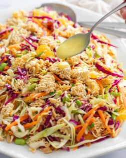 Ramen Noodle Salad on a white platter with a spoon drizzling dressing on top.