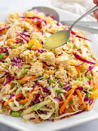 Ramen Noodle Salad on a white platter with a spoon drizzling dressing on top.