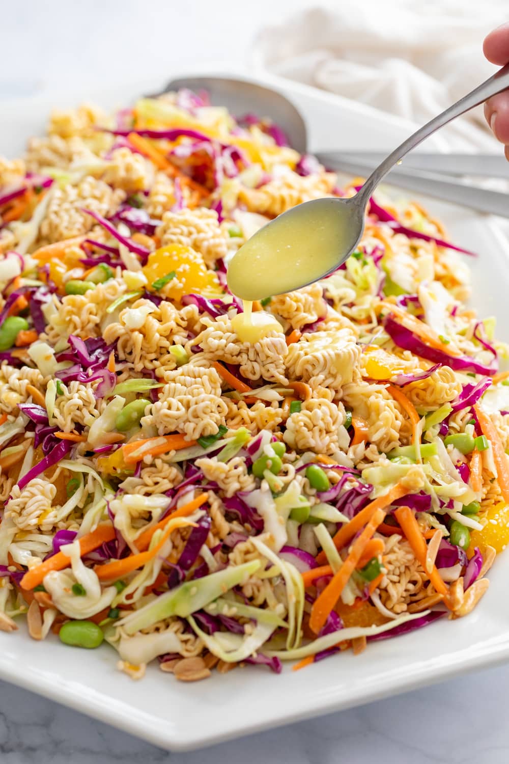 Ramen Noodle Salad on a white platter with a spoon drizzling dressing on top.
