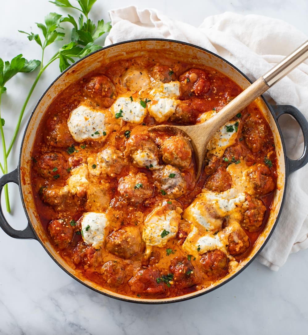 Ricotta Meatballs in a skillet with sauce, ricotta cheese, and a wooden spoon.