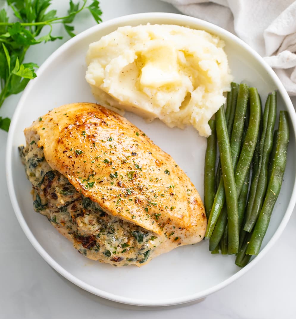 Stuffed Chicken Breast on a white plate with mashed potatoes and green beans.