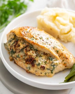 Stuffed Chicken Breast with mashed potatoes in the background and green beans on the side.