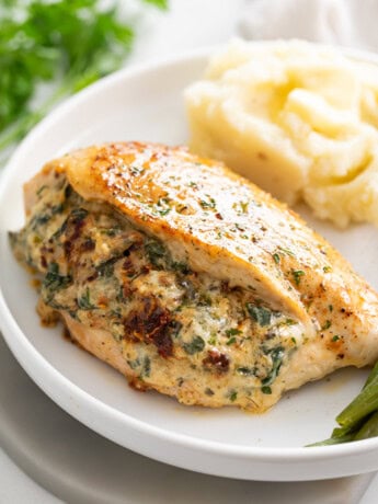 Stuffed Chicken Breast with mashed potatoes in the background and green beans on the side.