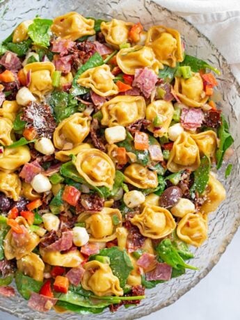 Tortellini Pasta Salad in a glass bowl with spinach, salami, mozzarella, and more.