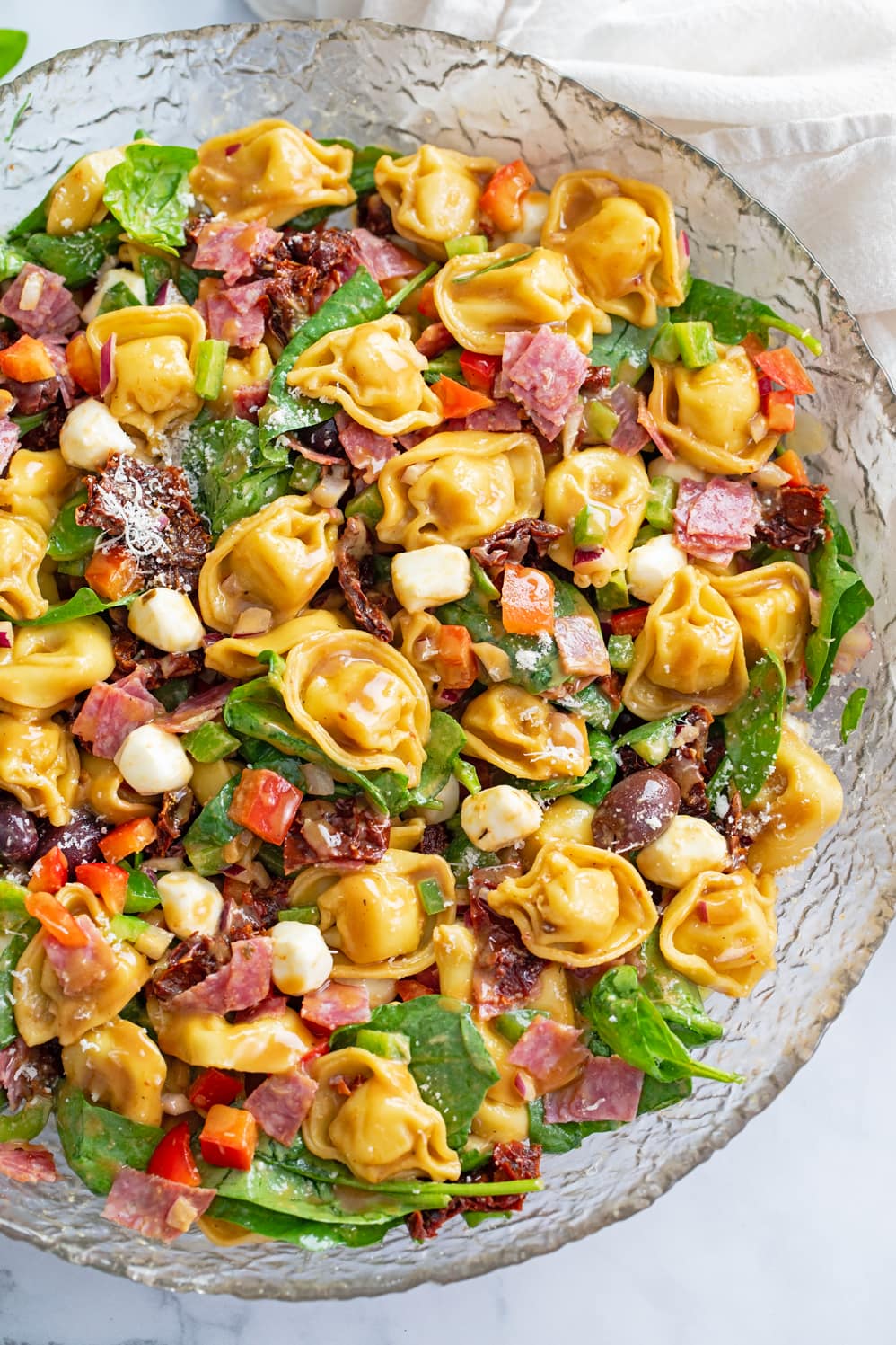 Tortellini Pasta Salad in a glass bowl with spinach, salami, mozzarella, and more.