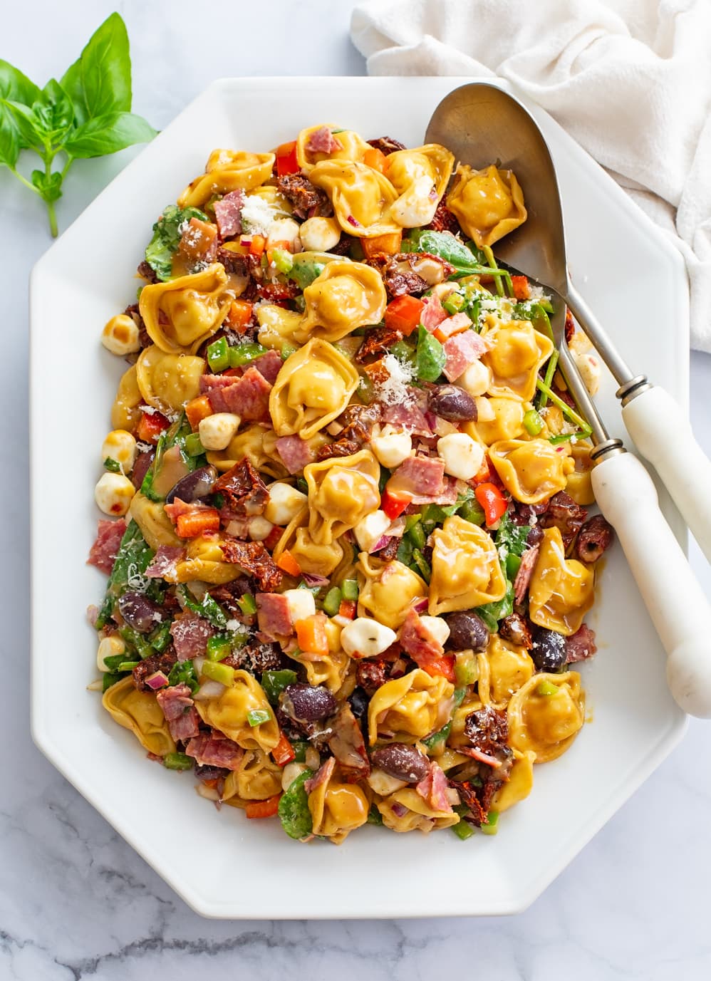 Tortellini Pasta Salad on a white platter with serving spoons on the side.