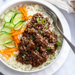 Korean Beef Bowls with ground beef in sauce over white rice next to cucumbers and carrots.