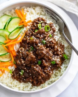 Korean Beef Bowls with ground beef in sauce over white rice next to cucumbers and carrots.