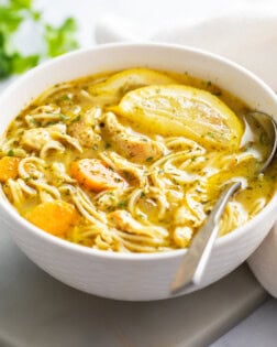 A white bowl of Lemon Chicken Soup with a spoon on the side.