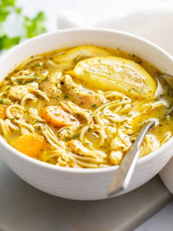 A white bowl of Lemon Chicken Soup with a spoon on the side.