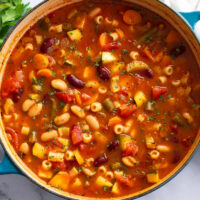 A soup bowl filled with Minestrone Soup with vegetables and beans.