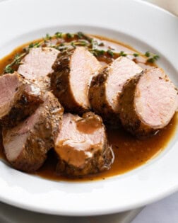 Slices of Roasted Pork Tenderloin on a white plate with pan sauce and thyme.