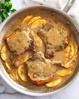 Apple Pork Chops in a skillet with sliced apples and sauce.