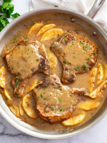 Apple Pork Chops in a skillet with sliced apples and sauce.