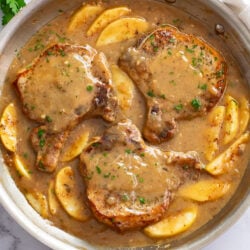 Apple Pork Chops in a skillet with sauce and sliced apples.