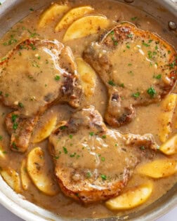 Apple Pork Chops in a skillet with sauce and sliced apples.