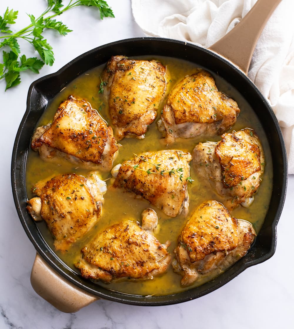 Baked Chicken Thighs in a skillet with sauce and parsley on the side.