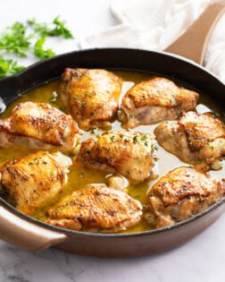 Baked Chicken Thighs in a skillet with pant sauce and fresh thyme on top.