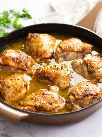 Baked Chicken Thighs in a skillet with pant sauce and fresh thyme on top.