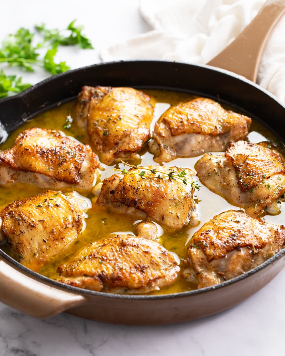 Baked Chicken Thighs in a skillet with sauce and fresh thyme on top.