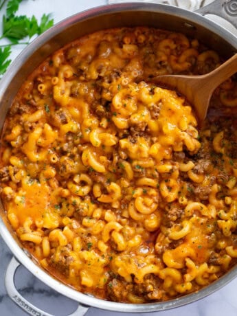 A skillet of Beefaroni with a wooden spoon in it.