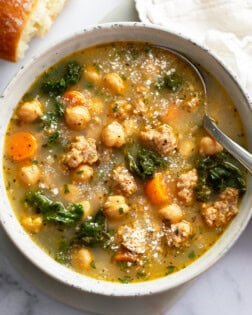 A bowl of Chickpea Soup with a spoon on the side and Parmesan cheese on top.