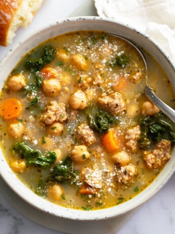 A bowl of Chickpea Soup with a spoon on the side and Parmesan cheese on top.