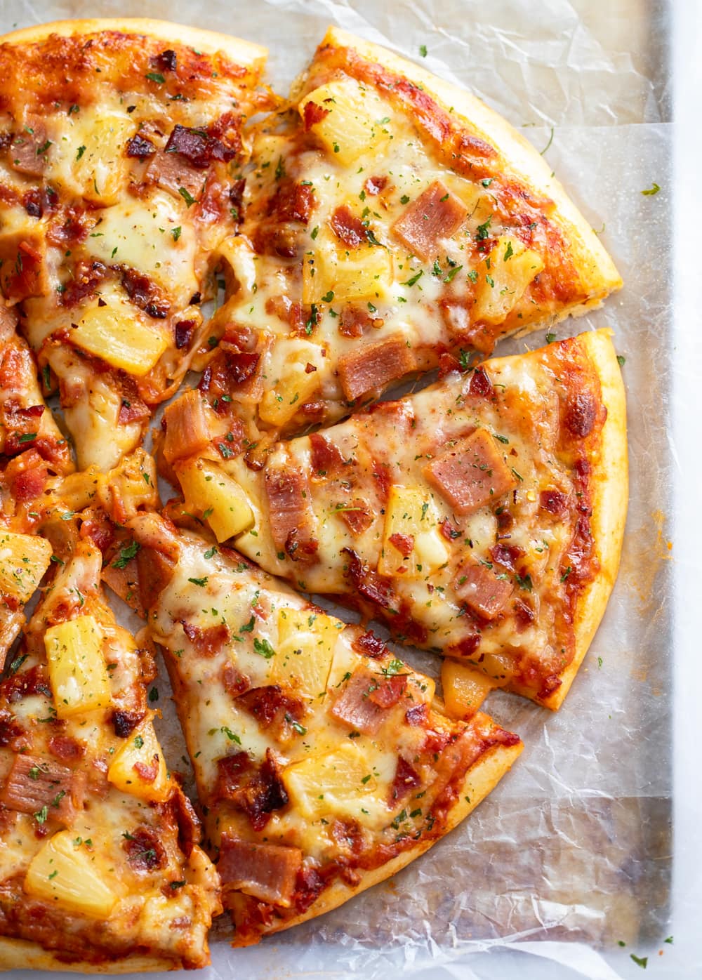 Hawaiian Pizza cut into slices topped with cheese, ham, bacon, and pineapple.