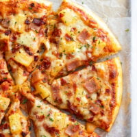 Slices of Hawaiian Pizza topped with pineapple, ham, bacon, and cheese.