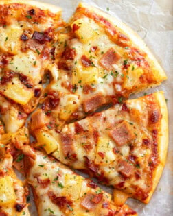 Slices of Hawaiian Pizza topped with pineapple, ham, bacon, and cheese.