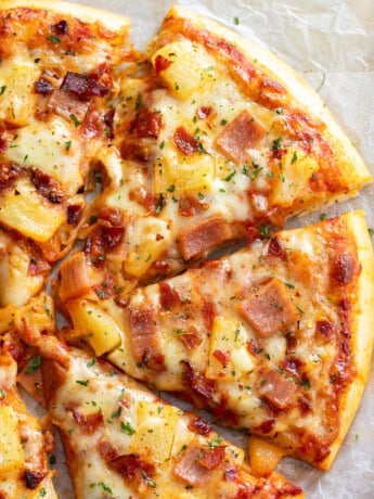 Slices of Hawaiian Pizza topped with pineapple, ham, bacon, and cheese.