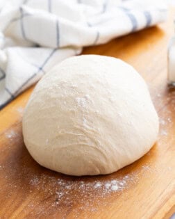 A ball of pizza dough topped with flour on a wooden surface.