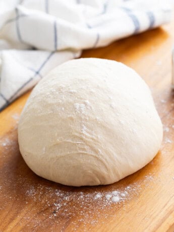 A ball of pizza dough topped with flour on a wooden surface.