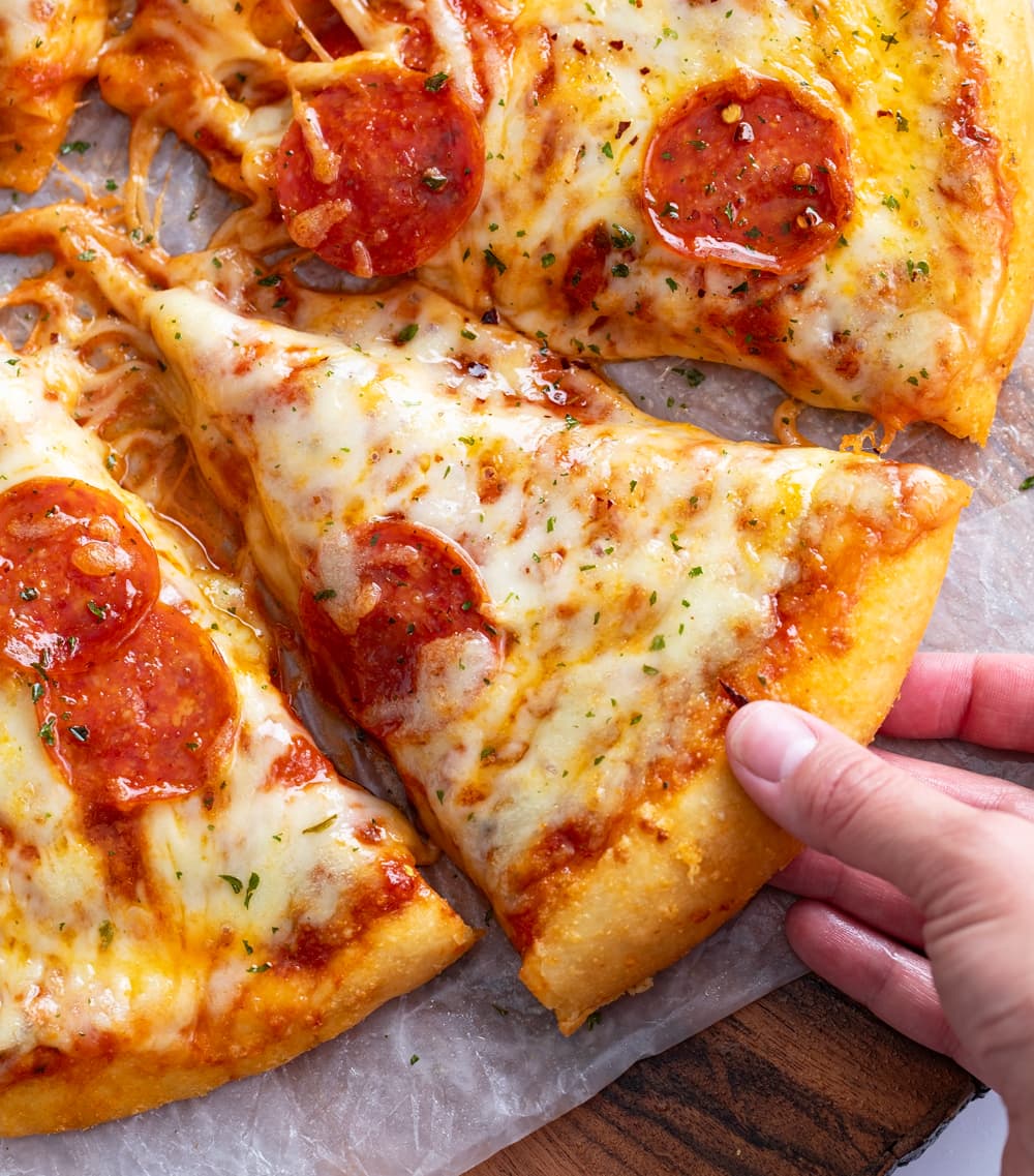 A hand pulling a slice of pepperoni pizza from a pizza pie.