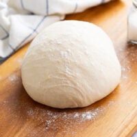 A ball of pizza dough on a wooden surface with flour sprinkled around it.