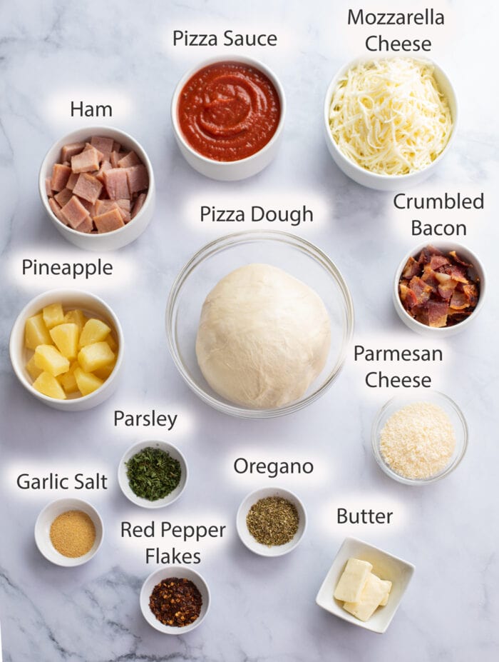 Labeled ingredients for making Hawaiian Pizza on a white surface.