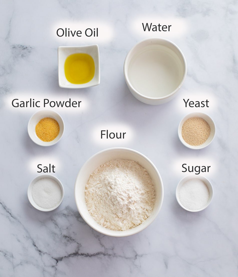 Labeled Ingredients for making pizza dough on a white surface.