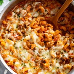 Italian Sausage Pasta in a skillet with a wooden spoon scooping it up.