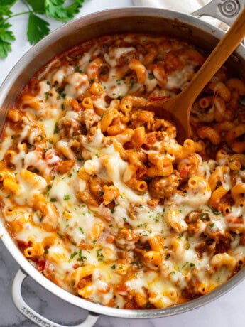 Italian Sausage Pasta in a skillet with a wooden spoon scooping it up.