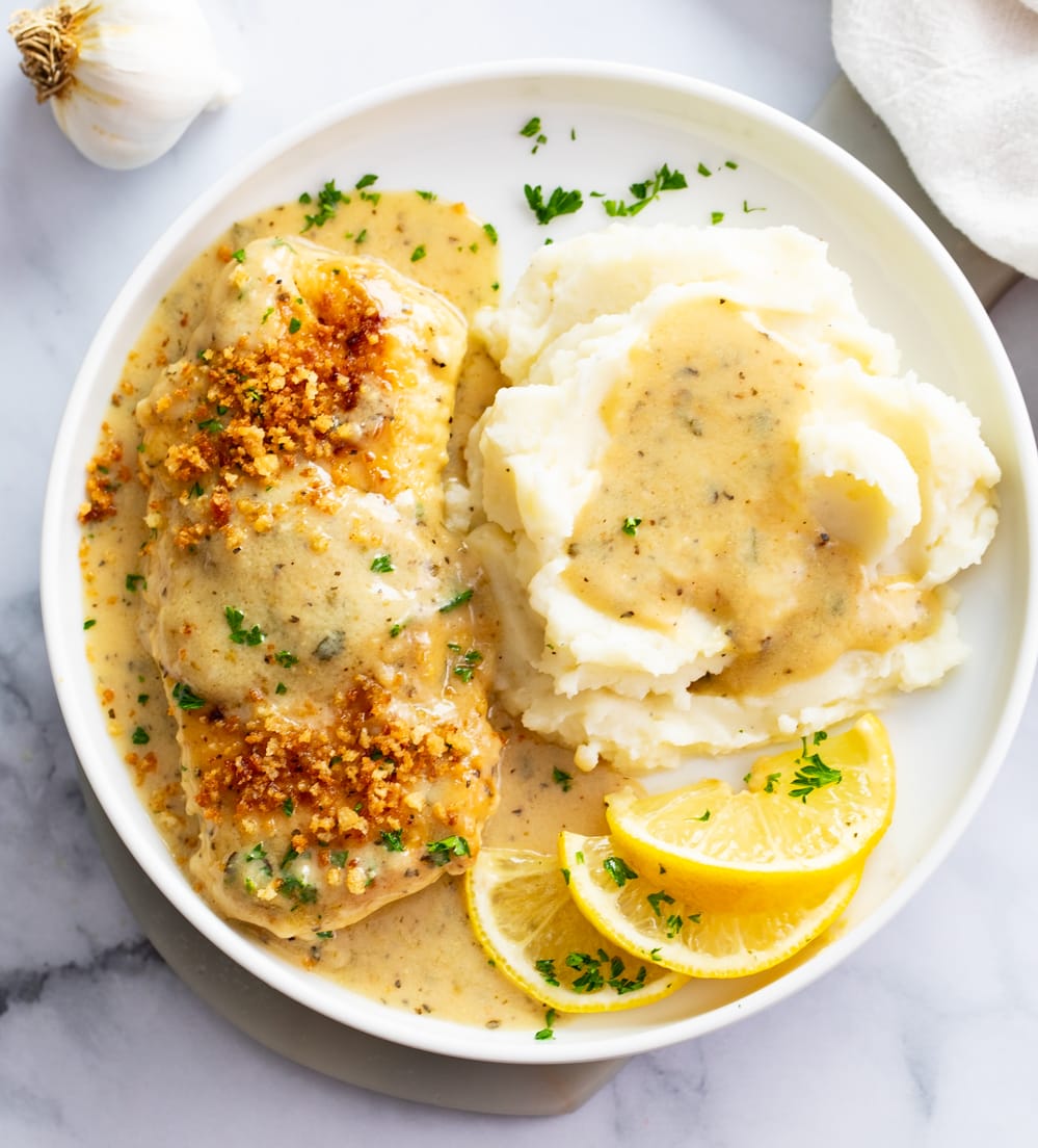 Lemon Garlic Chicken on a white plate with mashed potatoes and lemon slices.
