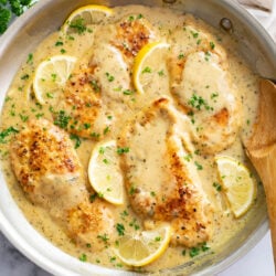 Lemon Garlic Chicken in a skillet with sauce, lemon slices, and parsley.